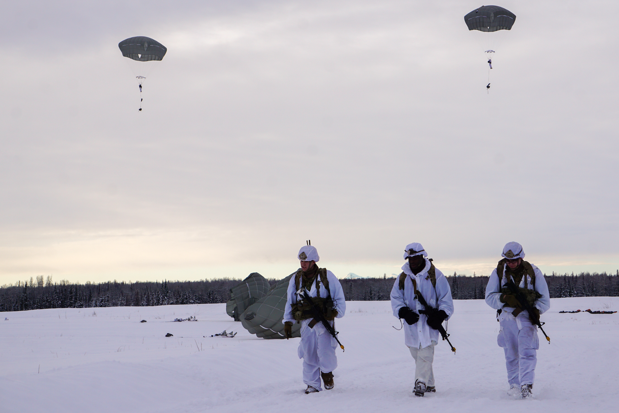 Three paratroopers walk across a snowy field.