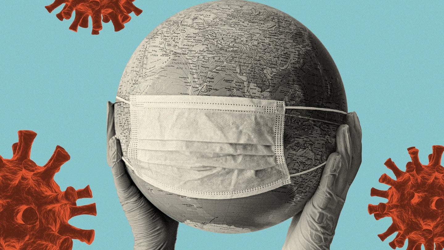 two gloved hands hold up a black and white globe with a medical mask stretched over it against a blue background with several red coronaviruses on it