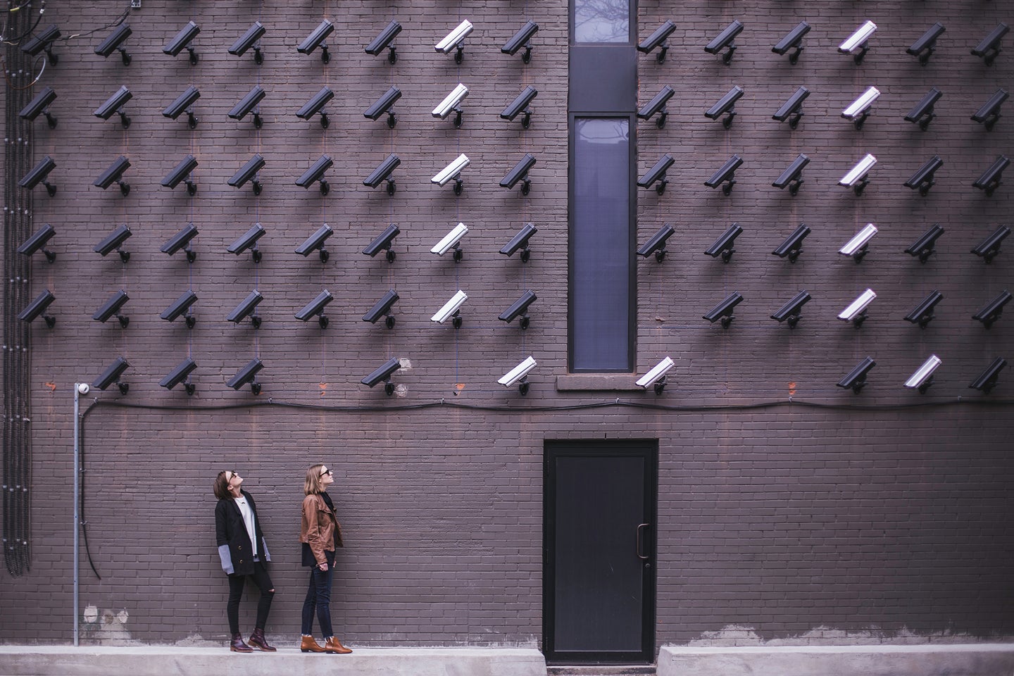 two people looking up at a lot of black and white security cameras mounted on a wall
