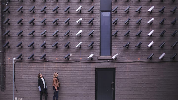 two people looking up at a lot of black and white security cameras mounted on a wall