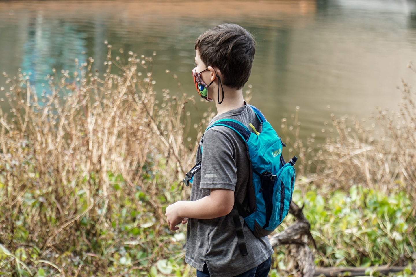 Kid with mask and backpack next to a pond