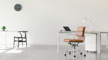 sparse office space with two desks, a black chair, a brown rolling chair, and white office cabinets