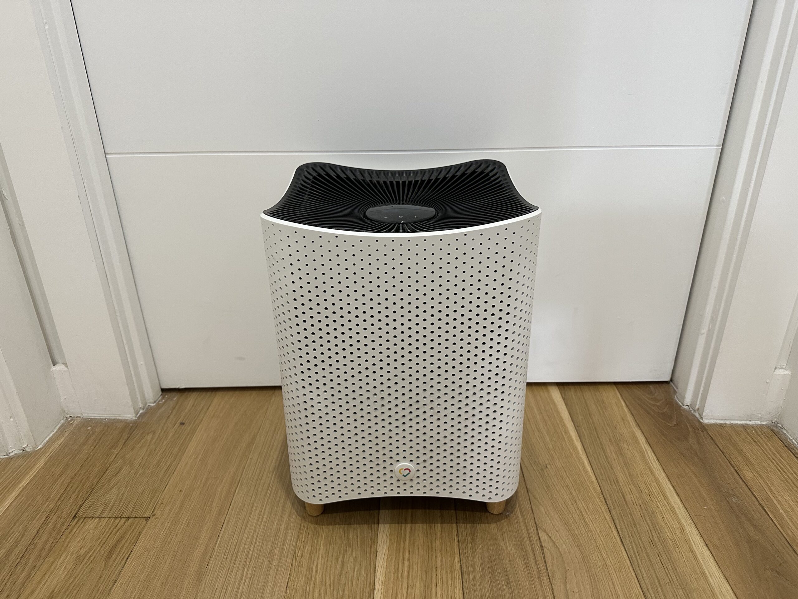 Mila smart air purifier on a light wooden floor in front of a closed white door