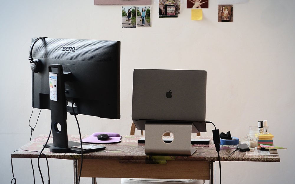computer desk with laptop on a stand and photos on the wall behind it