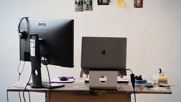 computer desk with laptop on a stand and photos on the wall behind it