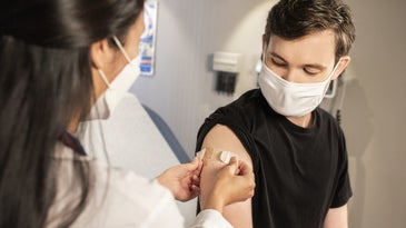 Young person receiving vaccine from healthcare worker while wearing a mask.
