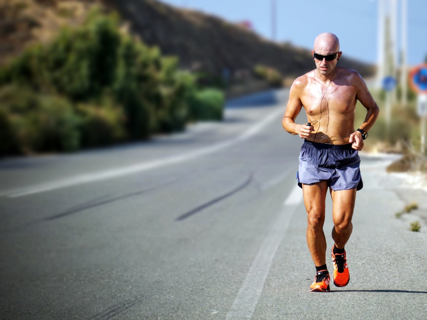 A man running shirtless on the side of a road in hot weather.