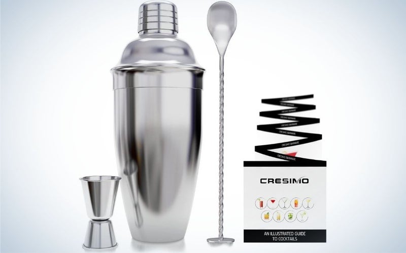 The silver Cresimo 24 ounce cocktail shaker bar set with accessories - Martini Kit with Measuring Jigger and Mixing Spoon plus drink recipes booklet beside it.