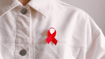 Person in white jacket wearing a red HIV/AIDS ribbon.