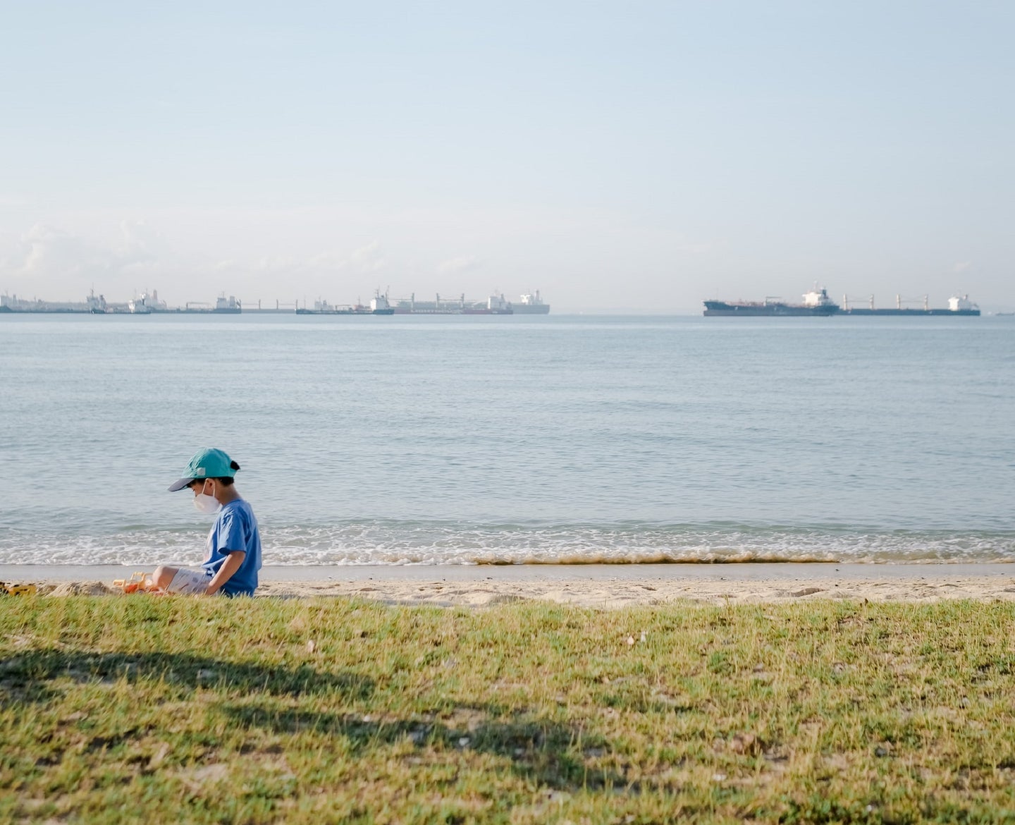 Kid in blue baseball cap and t-shirt sitting on a grassy beach