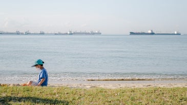 Kid in blue baseball cap and t-shirt sitting on a grassy beach