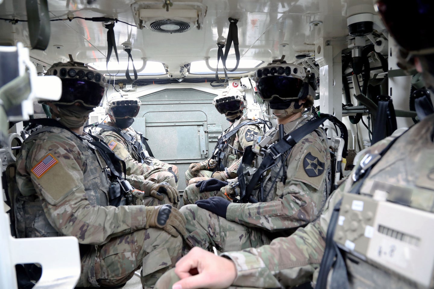 Soldiers wearing augmented reality headsets while sitting in a vehicle.