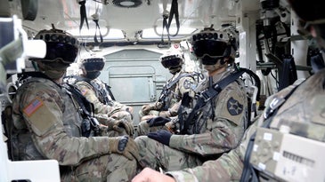 Soldiers wearing augmented reality headsets while sitting in a vehicle.