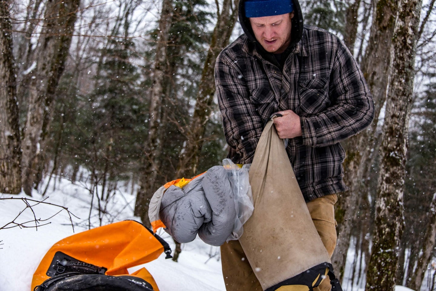 Person stuffing a sleeping bag and plastic bag in a compression bag in the snow