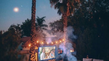 A film set with an outdoor projector with lights in the trees and the smoke of the burning fire.