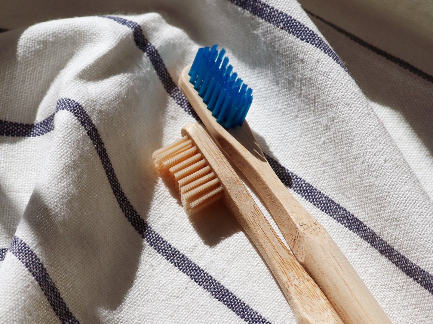 Two bamboo toothbrushes, one with tan bristles and one with blue bristles, on a white towel.