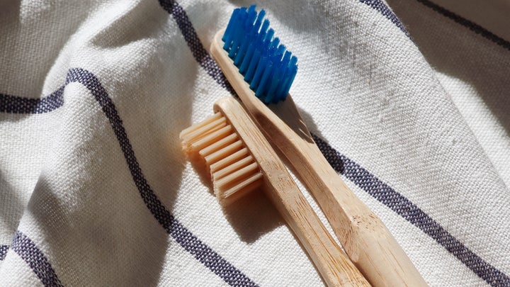 Two bamboo toothbrushes, one with tan bristles and one with blue bristles, on a white towel.