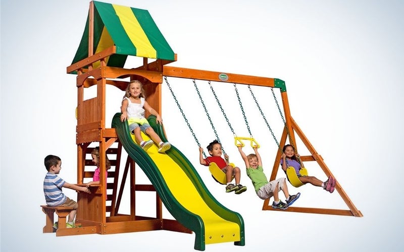 A wooden playset swing set with two standard belt swing set swings and a yellow and green swing trapeze bar into it.
