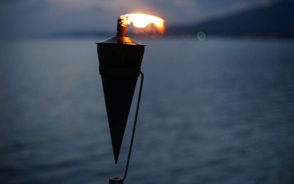 A black tiki torch with flame in a twilight sea background.