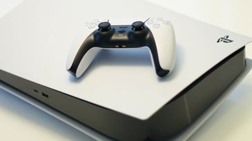A white-and-black PlayStation 5 controller on top of a white-and-black PS5.