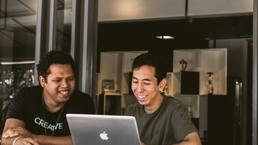 Two young brown people at a Mac laptop