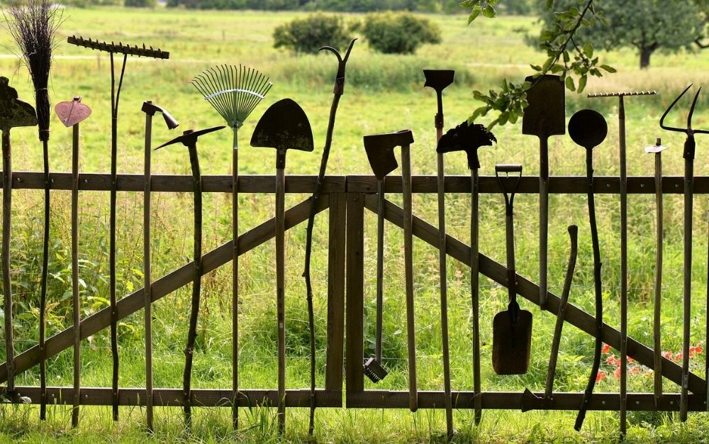 Different gardening tools standing on a wooden garden gate with garden background.
