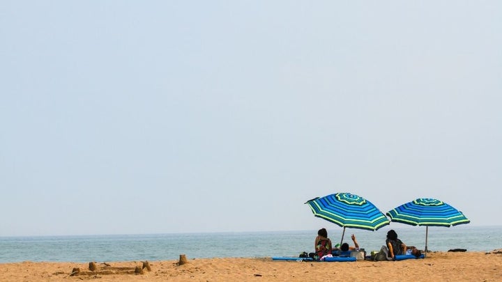 People lying down on the beach under their blue and green umbrella during daytime