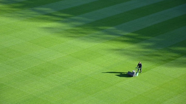 A man using a lawn mower in the middle of a large green field with grass.