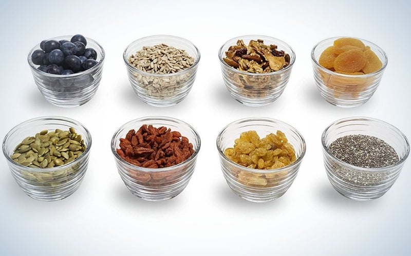 Eight small glass plates filled with different foods such as seeds or cereals, arranged in rows.