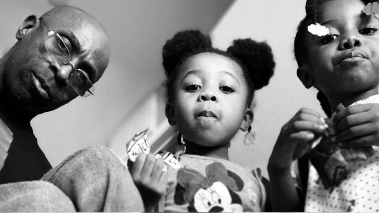 Black father and twin girls looking down at camera