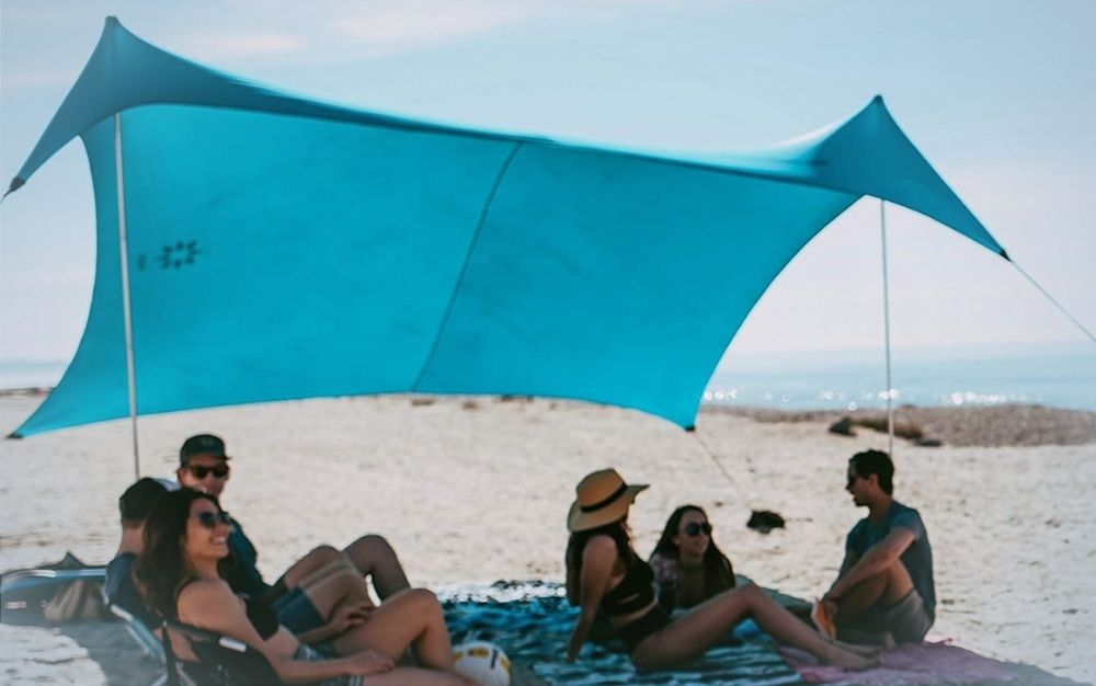 People sitting under a large sky blue beach tent