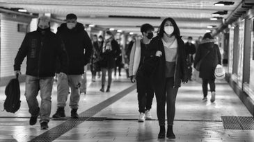 People with masks walk through long hallway.