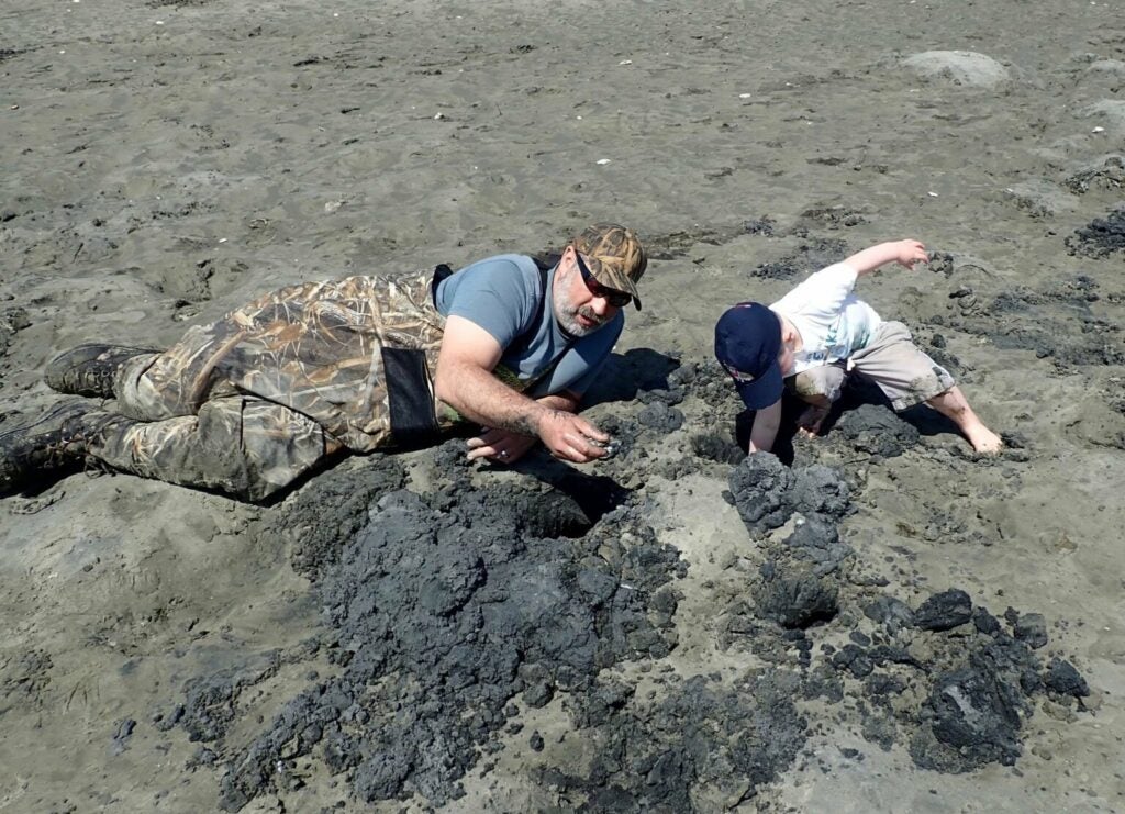 Man and child in camo overalls pulling clams out of sand