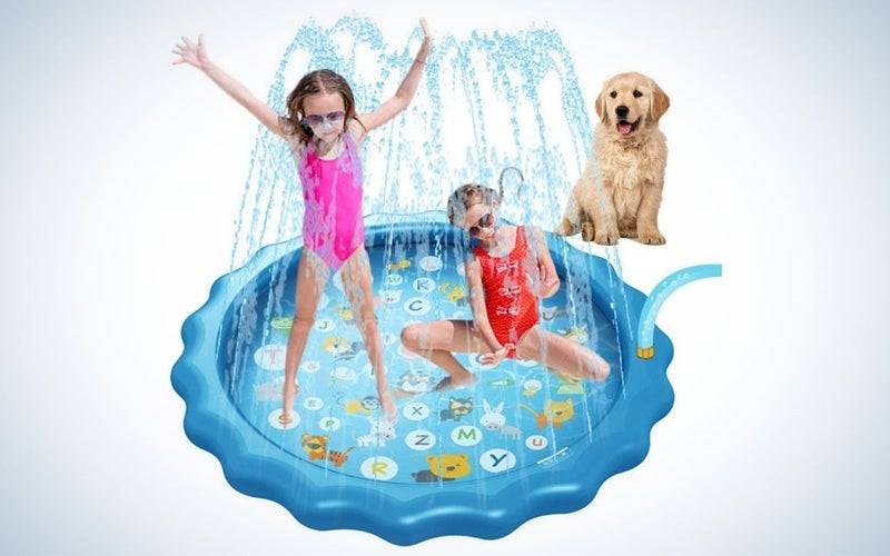 Two little girls playing on a blue splash pad and a dog looking at them