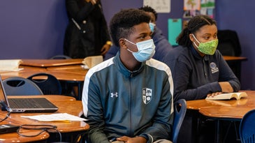 Black students in masks and track suits at desks