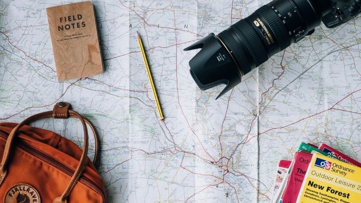 A map with the directions of the roads and over it a pencil, a professional camera, a notebook, and an orange bag.