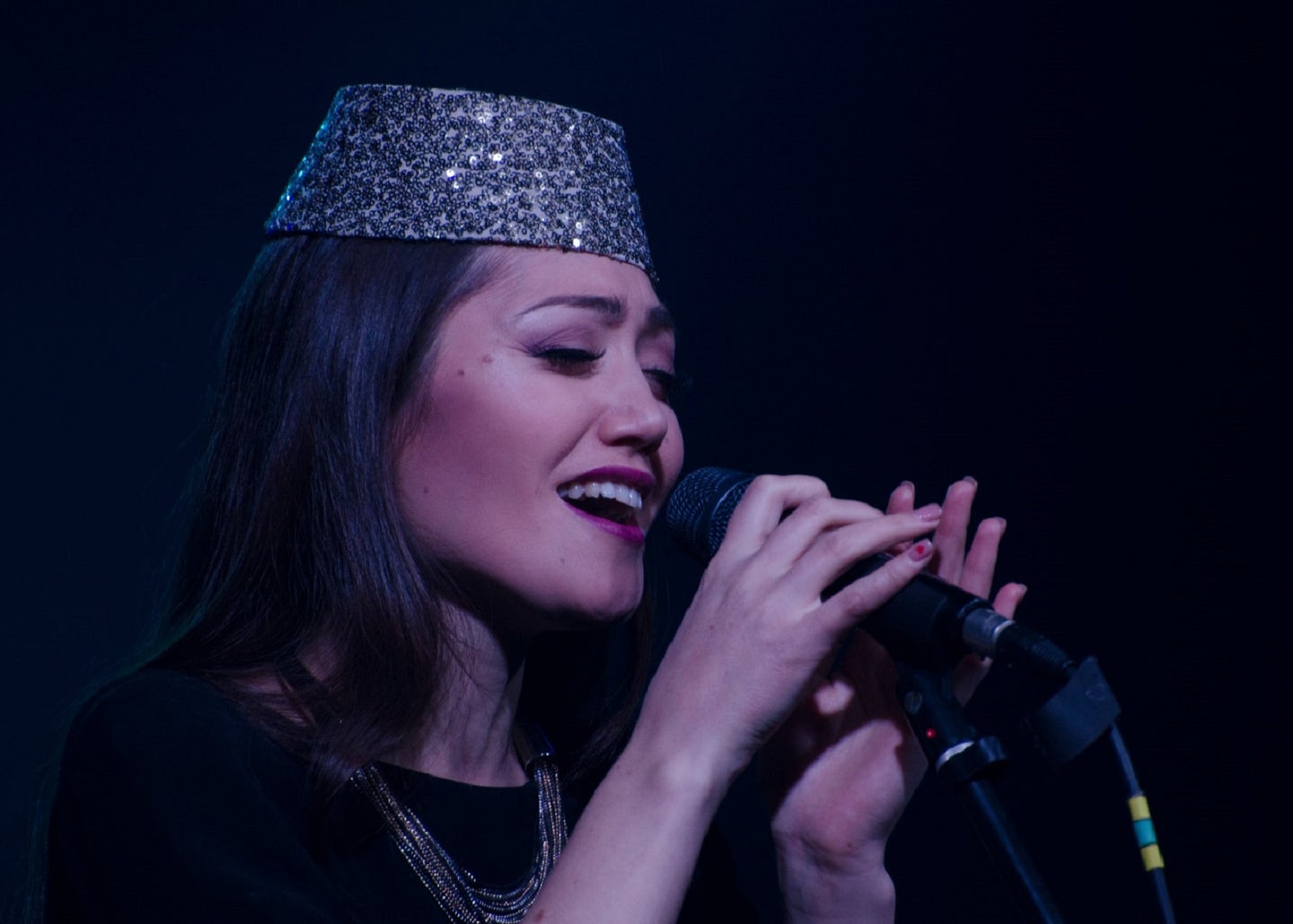 Person with long black hair and in silver sequin hat at microphone