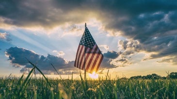 A USA flag waving under the sunset in a large green field.