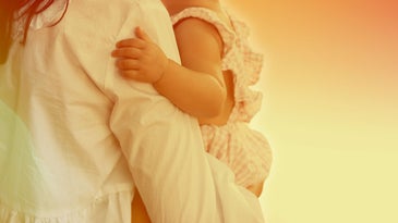 A person wearing a long-sleeved white shirt while holding a baby.