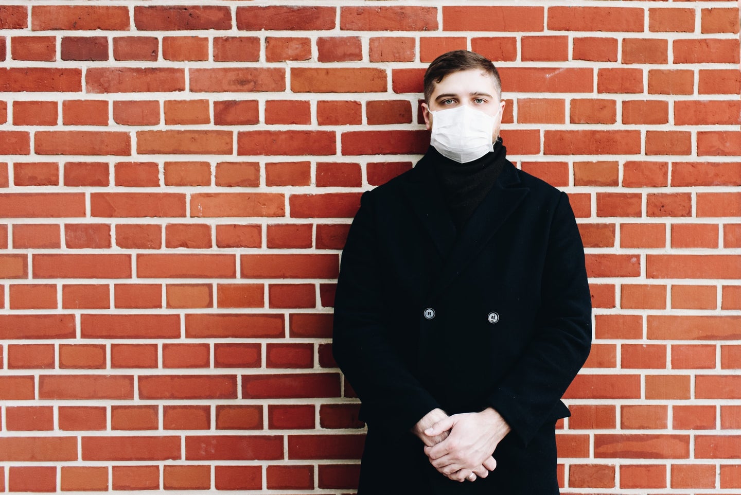 man in mask stands in front of brick wall