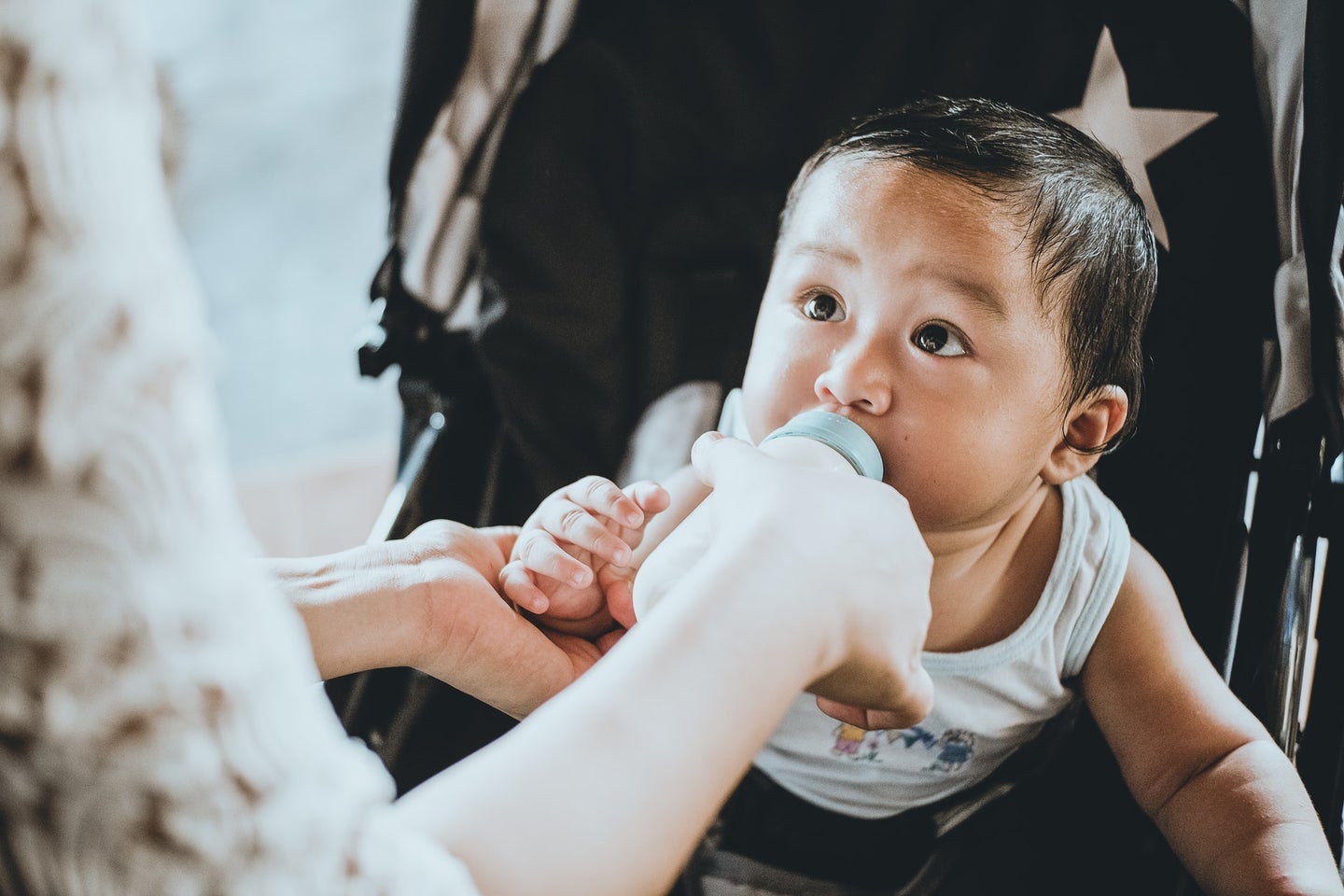 Baby with black hair being fed a bottle of milk