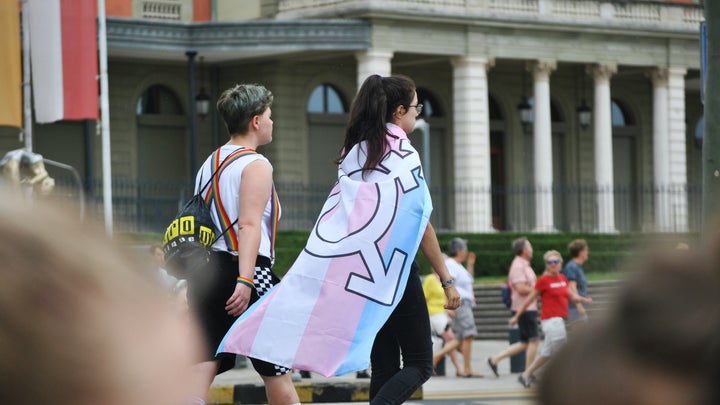 Teen with trans flag over shoulders walking with friend in rainbow pride suspenders