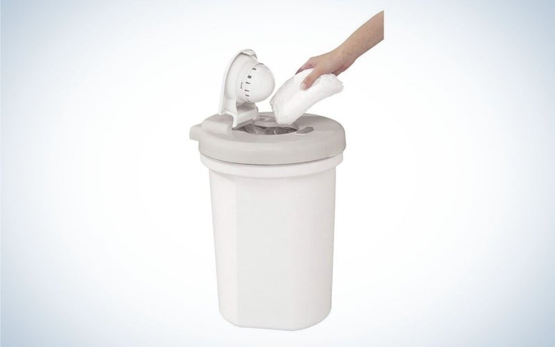 A cylindrical waste bin and all white plain and with a lid that opens from above and a hand that throws pampers inside it.