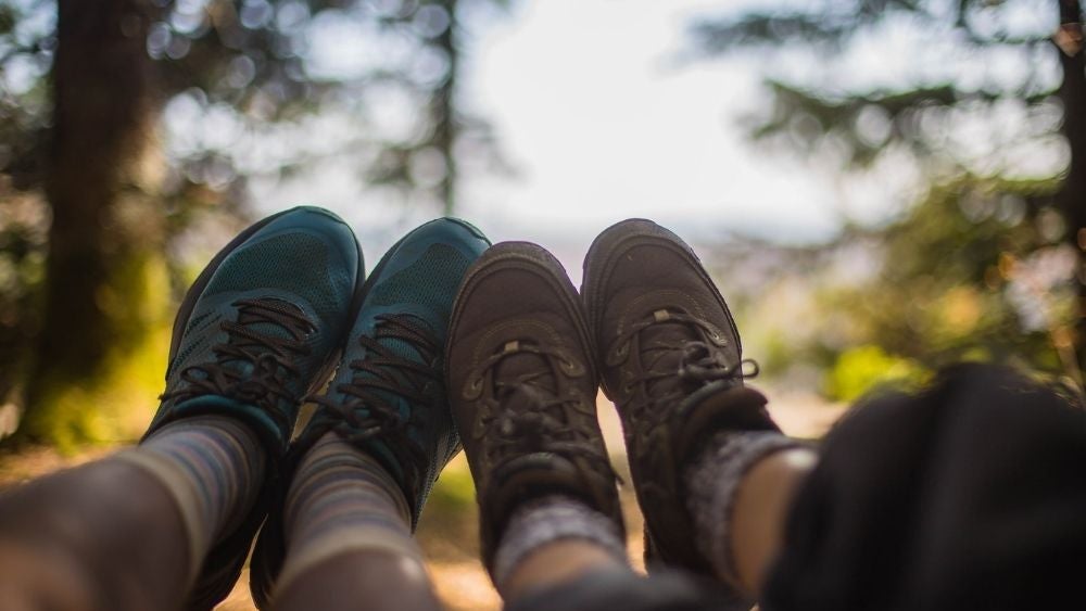 Two people wearing hiking boots, one blue and the other brown, and leaning close to each other.