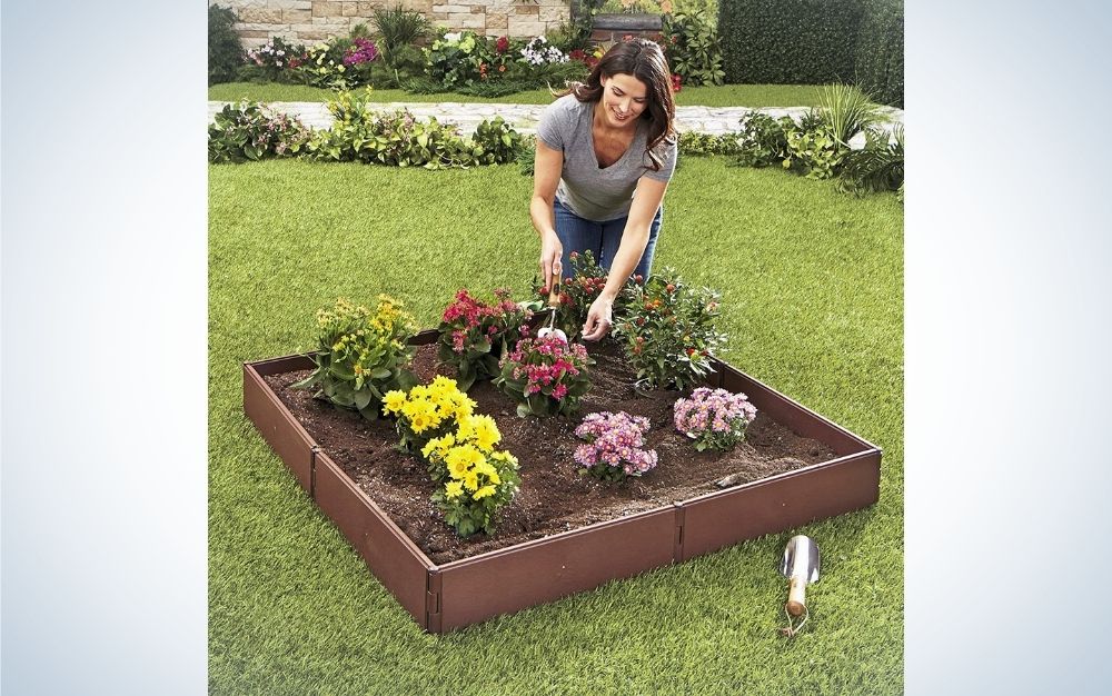 A woman taking care of her garden and flowers set in a square garden bed.