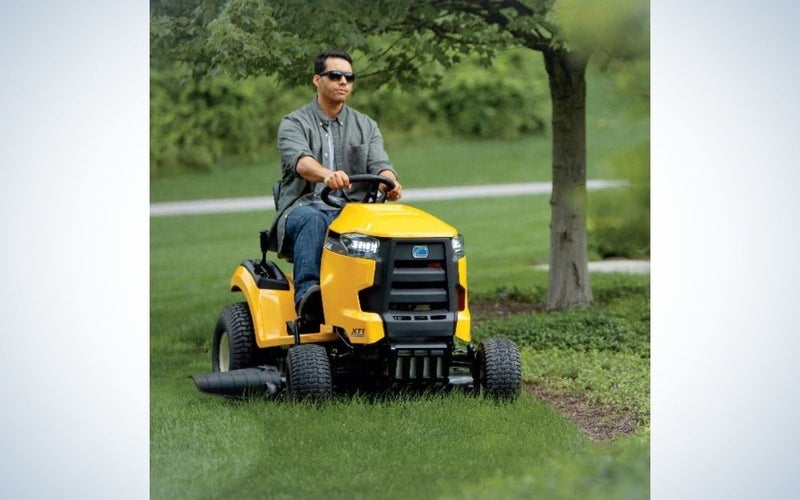 A man with eyes who drives a harvester on a green space with grass and flowers, which resembles an engine with four yellow and black tires.