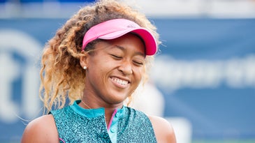 Naomi Osaka smiling on the tennis court in a pink visor