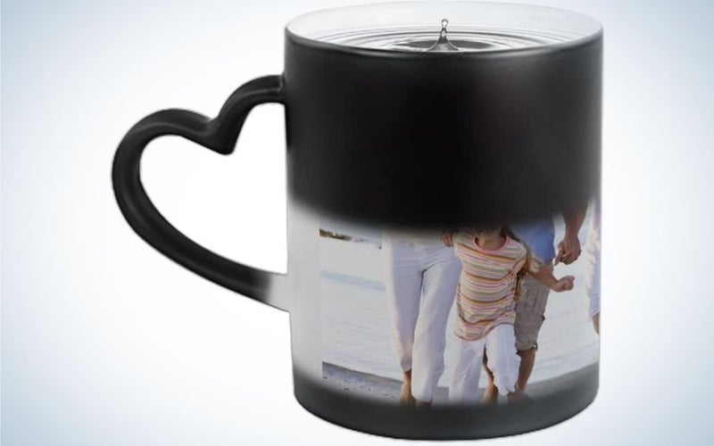 A black and white cup with a picture of a family printed on it and a heart-shaped tail in black.