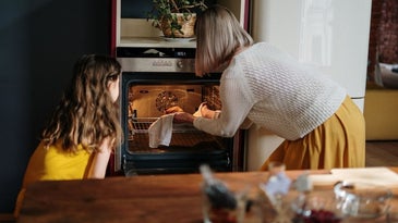 A woman with a little girl who is putting a pan in the oven with yellow light.