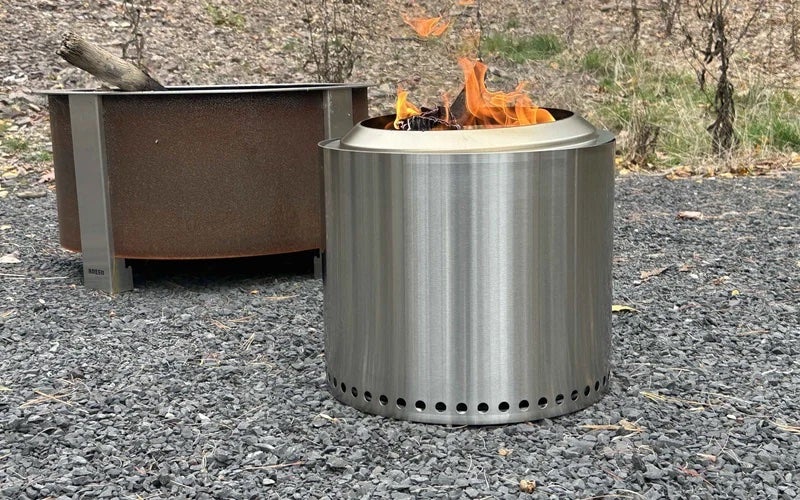 A stainless steel Solo Stove Ranger with flames coming out the top on a gravel driveway.